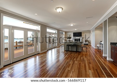 Luxury spacious family room interior with wall of glass doors leading out to spacious deck and facing the lake, polished hardwood floor and cozy sitting area with fireplace . Northwest, USA