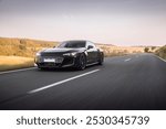 Luxury sports car driving on an open road surrounded by scenic countryside, showcasing sleek design and high performance on a clear, peaceful day