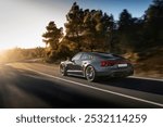 Luxury sports car driving at sunset on a winding road, surrounded by trees, showcasing speed, elegance, and high-performance in a scenic setting