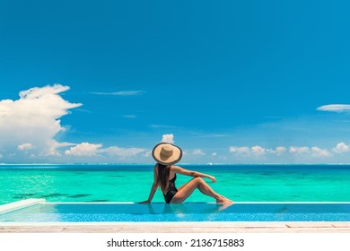 Luxury summer vacation tourist woman relaxing by swimming pool. Elegant lady relaxing sunbathing enjoying travel holidays at resort infinity overwater pool. Luxury lifestyle.