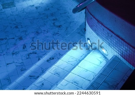 A luxury swimming pool with clearly transparent water and white marble tile floor. Building place photo, selective focus at marble tile. Photo contained some noise due to low light environment.