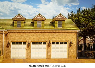 Luxury Three Car Garage With Carriage Lights Between Doors Set In Brick House With Green Wood Shingle Roof And Dormers