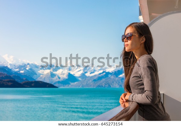 Luxury travel Alaska cruise vacation woman\
relaxing on balcony enjoying view of mountains and nature\
landscape. Asian girl sunglasses\
tourist.