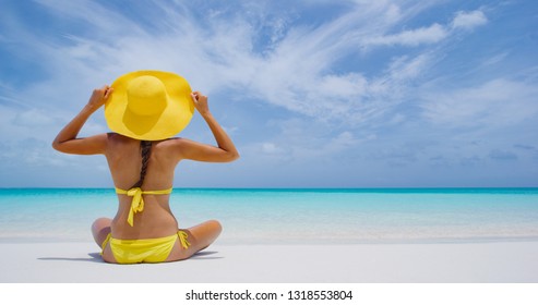 Luxury Travel. Beach woman enjoying serene luxury vacation relaxing under the sun looking at perfect turquoise water and ocean at tropical getaway paradise. Girl bikini model from the back sunbathing.