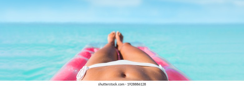 Luxury travel caribbean tropical beach vacation banner panoramic bikini woman sunbathing on air mattress. Legs suntan girl relaxing on inflatable swimming pool bed floating in turquoise ocean water.