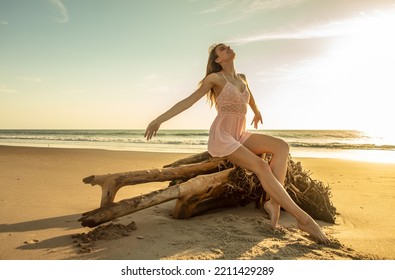 Luxury Travel Destination At Sunset With Young Caucasian Girl In Bohemian Dress Enjoying Summer Sun Sitting On Driftwood