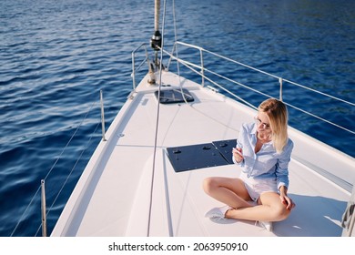 Luxury Travel On The Yacht. Young Happy Woman Using Smartphone On Boat Deck Sailing The Sea. Yachting And Technology.