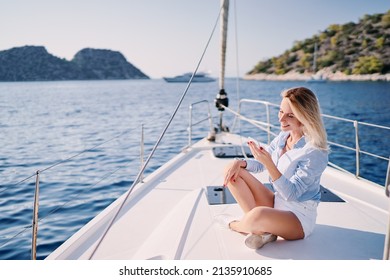 Luxury travel on the yacht. Young happy woman using smartphone on boat deck sailing the sea. Yachting and technology.