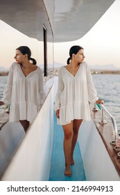 Luxury Travel On A Yacht. A Young Woman Enjoys The Sunset On The Deck Of A Boat Sailing The Sea. Beautiful Girl In A White Dress.