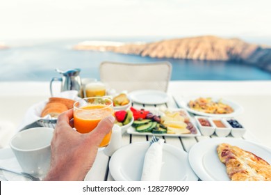 Luxury Travel Resort Breakfast In Room Service At Fancy Hotel Restaurant With Amazing Balcony View Over Santorini Island, Oia, Greece. Europe Vacation Food Selfie. Man Drinking Morning Orange Juice.