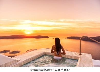 Luxury travel Santorini vacation woman swimming in hotel jacuzzi pool watching sunset. Europe resort destination holiday for honeymoon getaway.