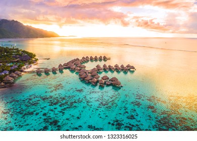 Luxury travel vacation aerial of overwater bungalows resort in coral reef lagoon ocean by beach. View from above at sunset of paradise getaway Moorea, French Polynesia, Tahiti, South Pacific Ocean.