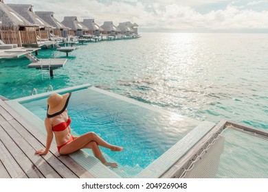 Luxury travel vacation in Bora Bora high end resort hotel tourist lady tanning in bikini by the swimming pool at overwater villa suite.