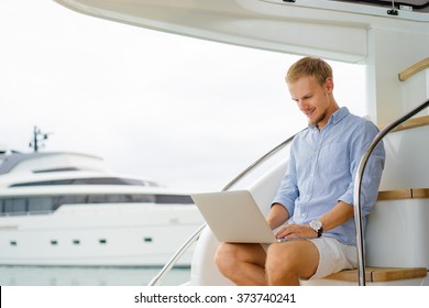 Luxury Traveling And Working. Handsome Young Man Using Laptop On The Deck Of Modern Yacht.