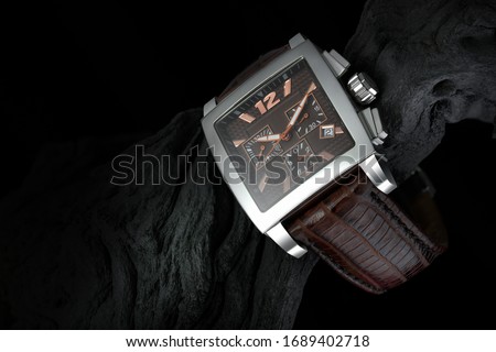 luxury watch on black wood with black background. The watch is made of precious metal and a crocodile strap. Commercial and product photo. A beautifully lit elegant men's watch. 
