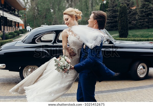 luxury wedding couple\
dancing at old car in light. stylish bride and groom hugging and\
embracing in city street. romantic passionate sensual moment. woman\
and man together