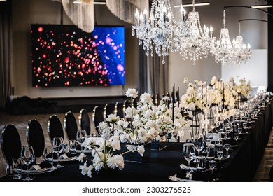 Luxury wedding reception. Trendy decor large chandelier for a birthday party. Table setting, setup. Banquet decoration composition flowers, candles in hall restaurant. Table covered black tablecloth.