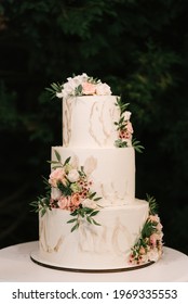 Luxury Wedding Tiered White Cake Decorated With Flowers, Photo At Night On The Background Of Lights