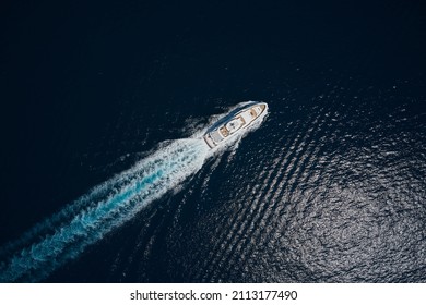 Luxury white mega yacht fast movement on dark water in the ocean top view. Big yacht in the sea drone view. Big white super boat moves on the water leaving a white trail aerial view.