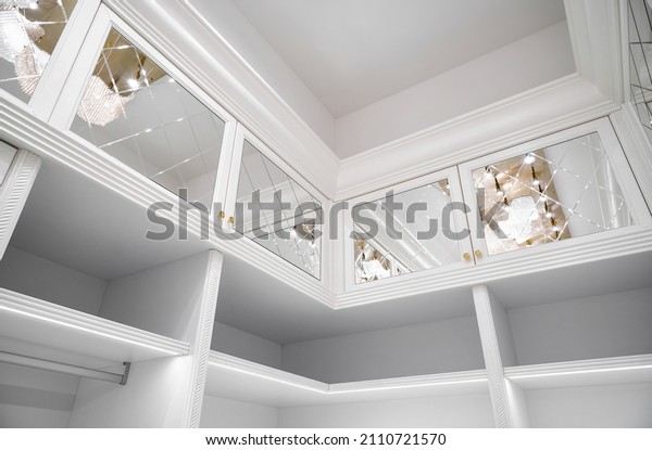 Luxury white walk-in closet with led lamps on\
shelves and mirror facades with rhombuses and contemporary luster\
in apartment