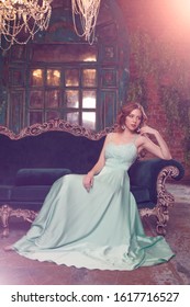 Luxury Woman Model In A Mint-colored Dress Sitting On A Vintage Couch. Beauty Girl With A Stunning Makeup And Hairstyle.