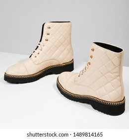 Luxury Women's Short Beige Quilted Autumn And Winter Boots With A Gold Chain On The Sole, Stand On A Gray-white Background With Shadow