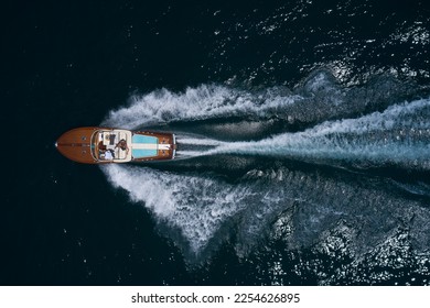 luxury wooden big motorboat with people fast moving on dark water top view