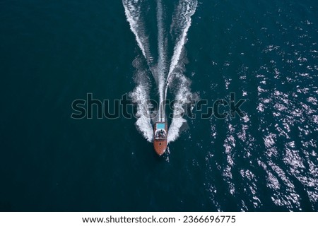 Luxury wooden big speedboat fast moving on dark water top view. Expensive wooden big boat with people moving on the water aerial view. Boat movement on the water. Motor boat in motion.