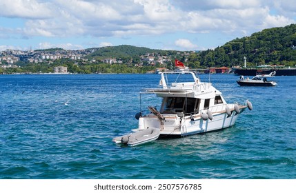 A luxury yacht anchored in the blue waters of the Bosphorus, with Istanbul's lush hills and historic architecture in the background - Powered by Shutterstock