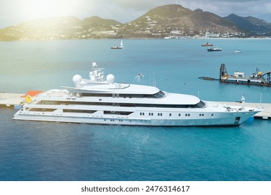 A luxury yacht docked in clear Caribbean waters with scenic hills in the background - Powered by Shutterstock