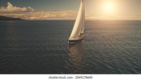 Luxury yacht race in open sea with sun reflections. Serene seascape with sailboat. Yachting at ocean bay water. Cinematic summer cruise at Arran Island, Scotland, Europe. Aerial panorama view - Shutterstock ID 2049178640