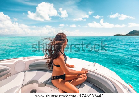 Luxury yacht woman enjoying freedom on deck in the wind relaxing on high end boat summer vacation trip upscale lifestyle of young rich people. Elegant black bikini, long hair and sun tanned body.