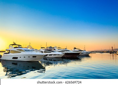 Luxury yachts docked in sea port at sunset. Marine parking of modern motor boats and blue water. Tranquility, relaxation and fashionable vacation.