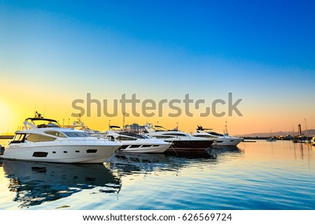 Luxury yachts docked in sea port at sunset. Marine parking of modern motor boats and blue water. Tranquility, relaxation and fashionable vacation.