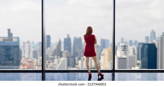 Luxury Young Asian CEO Woman Entrepreneur Looking At The Downtown Skyline At The Window With Skyscraper And Cityscape For Vision And Real Estate Development Concept