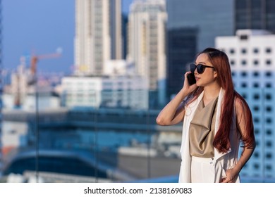 Luxury Young Asian CEO Woman Entrepreneur Using Mobile Phone With Skyscraper And Cityscape On The Background For Business Communication And Urban Lifestyle Concept 