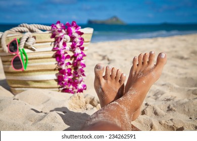 Luxury young woman legs and feet sunbathing on a tropical Hawaiian beach