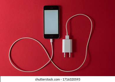Lviv, Ukraine - April, 28.2020: iPhone is connected to the charger on a red background.