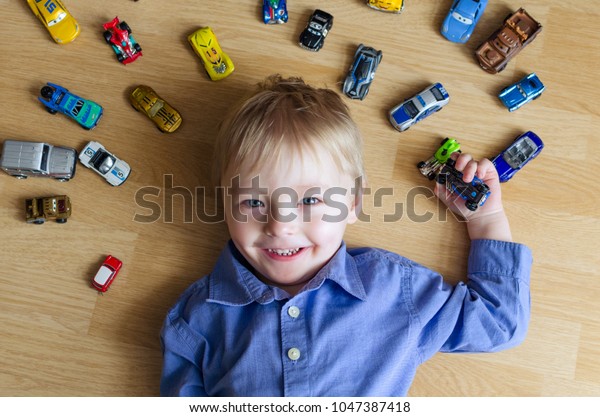 LVIV,\
UKRAINE - FEBRUARY 15, 2018: Happy boy lying on the floor with toy\
cars around him. Smiling kid playing with his model car collection.\
Toy mess in kids room. Many cars for little\
boys.