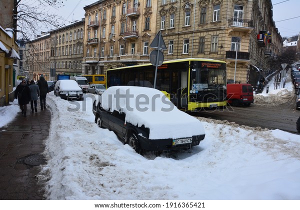 Lviv.\
Ukraine. February 2021.Snow covered cars after snowfall at winter\
day.Vehicles covered with snow in a winter blizzard in the parking\
lot. Snow-covered roads and streets of the\
city.