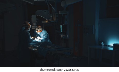 Lviv, Ukraine - February 8, 2022: Doctors In Dark Operating Hospital Room Perform Surgery. Dark Background. Operation In Modern Hospital. Innovation Technology System. Professional Doctor Group.