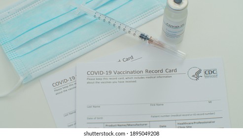 Lviv, Ukraine - January 14, 2021: Medical Mask And COVID-19 Vaccine On Vaccination Record Card Approved By CDC With Corona Virus Vaccine Vials. White Background.