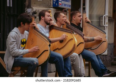 Lviv, Ukraine - July 10, 2022: Group Of Four Young Men Singing And Playing Bandura, Ukrainian Plucked String Folk Instrument. Gritty Street Style Photo