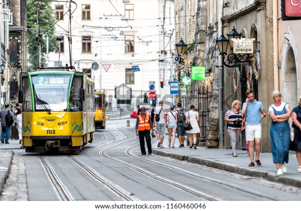 Lviv, Ukraine - July 30, 2018: Conductor man standing\
by trolley tram in historic Ukrainian Polish city in old town with\
crowd of people, rail tracks, wires coffee cafe shops, restaurants\
during day