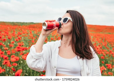 Lviv, Ukraine - Jun 11, 2020: Woman Drinking Coca Cola Standing At The Field Of Poppy Flowers. Hot Summer Day