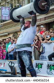 LVIV, UKRAINE - JUNE 2016: Athlete strongman inflated with athletic body lifting heavy barbell on a city street