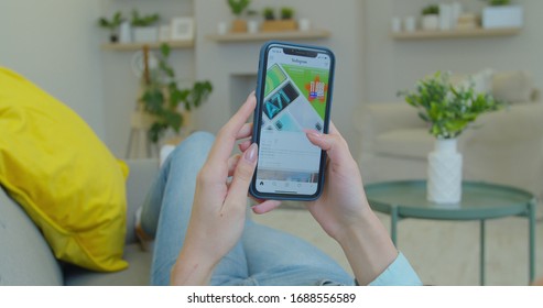 LVIV, UKRAINE - March 5, 2020: Woman At Home Lying On A Couch Using Smartphone Scrolling Through Instagram Feed, Doing Swiping, Scrolling Gestures.