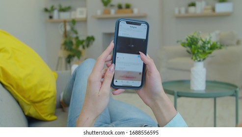 LVIV, UKRAINE - March 5, 2020: Woman At Home Lying On A Couch Using Smartphone Scrolling Through Instagram Feed, Doing Swiping, Scrolling Gestures.