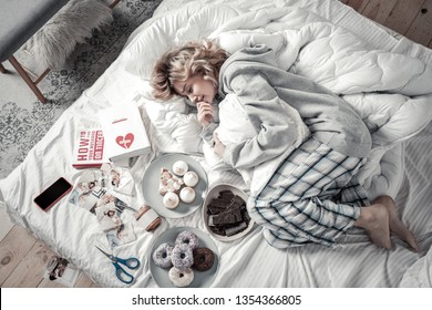 Lying In Bed. Emotional Woman Wearing Pajamas Lying In Bed Near Books And Food After Breakup