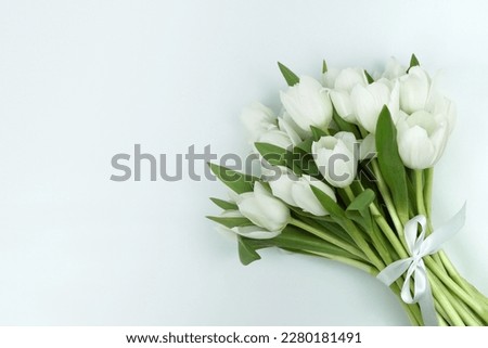 Lying bouquet of white tulips with a white bow on the right of the picture, white background, free space on the left, horizontal